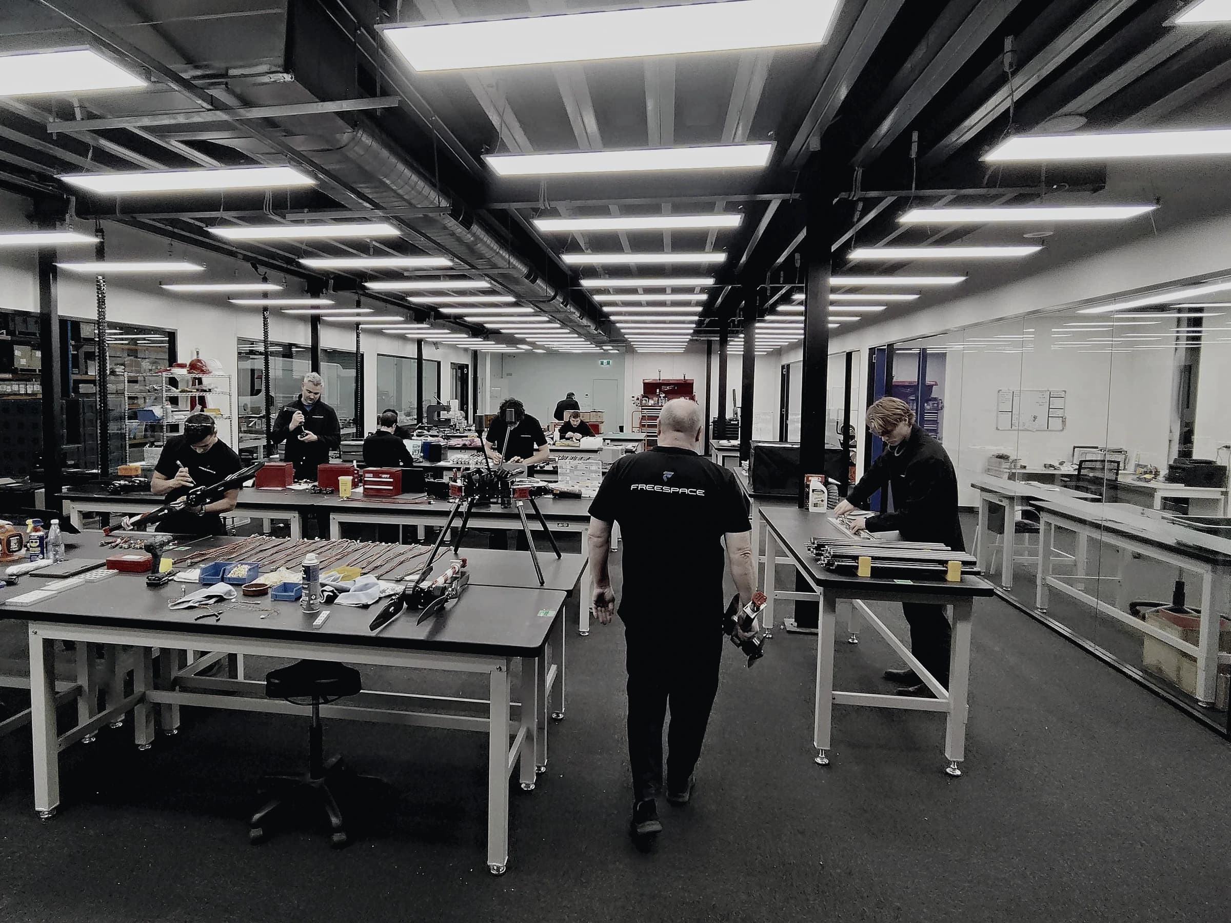 The Freespace build floor, technicians at rows of benches assembling Callisto arms and airframes