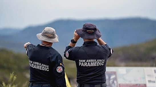 Two NSW Ambulance paramedics at a lookout, one pointing out across the valley to the ranges