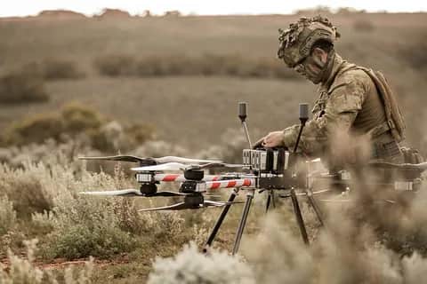 An Australian Army soldier kneeling beside a Callisto in dry scrub, preparing it for flight