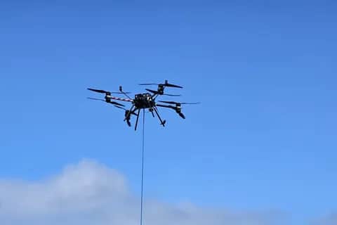 A Callisto 50 in flight against a blue sky, a line hanging beneath it