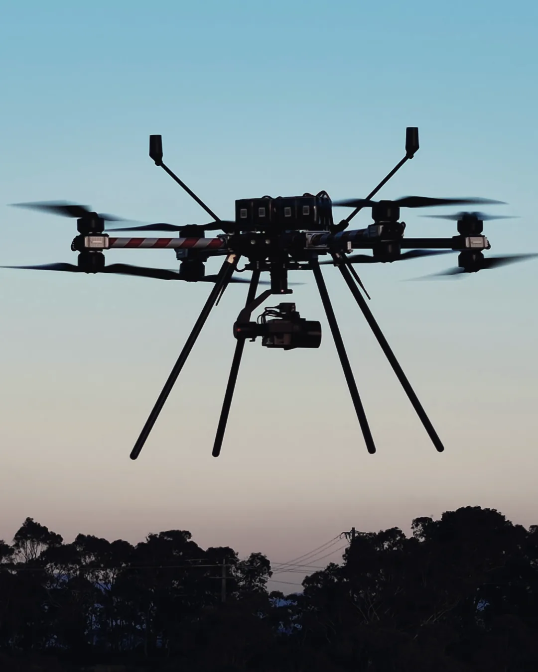 A Callisto 50 with its gimbal camera hovering against a dusk sky above a treeline