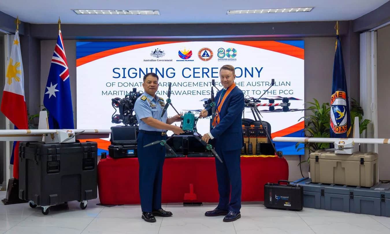 A Philippine Coast Guard admiral and an Australian official shaking hands at the signing ceremony, the Callisto kit on the table before them
