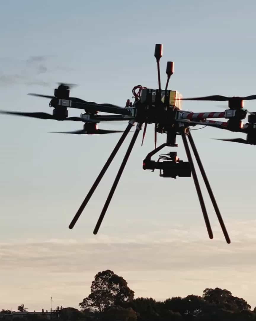 A Callisto hovering against an evening sky, the view up from beneath it as it tows a red line across a field, a Callisto pulling line past a transmission tower's insulator, and the aircraft silhouetted against the setting sun