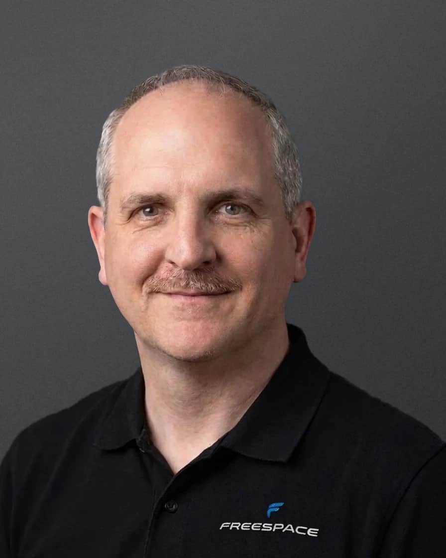 Ken King, head and shoulders, in a black Freespace polo against a soft grey studio backdrop
