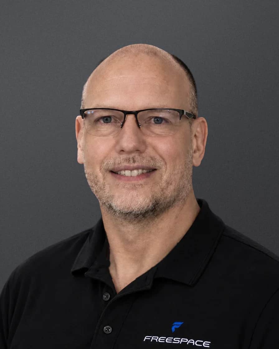 Leonard Hall, head and shoulders, wearing glasses and a black Freespace polo against a soft grey studio backdrop
